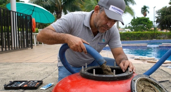 Un técnico de piscina inserta una manguera de aspiración en un filtro de arena rojo para limpiarlo.